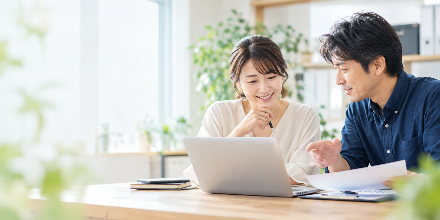 明るいオフィスで、ノートパソコンを見ながら打ち合わせをする女性と男性